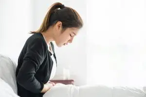 woman sitting bed with abdominal pain pressing her hand her stomach