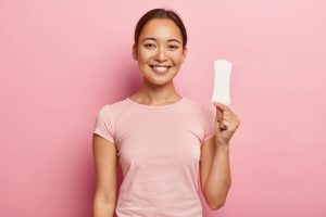 photo attractive young lady with asian appearance holds clean sanitary napkin satisfied with its quality uses intimate product during menstruation periods isolated pink wall